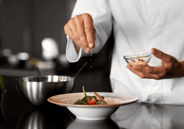 Chef de cozinha salpicando sal sobre um prato com folhas verdes e tomate cereja.
