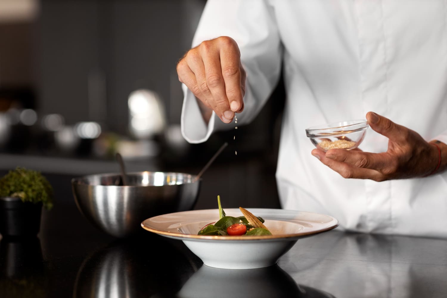  Chef de cozinha salpicando tempero sobre uma salada em prato branco.