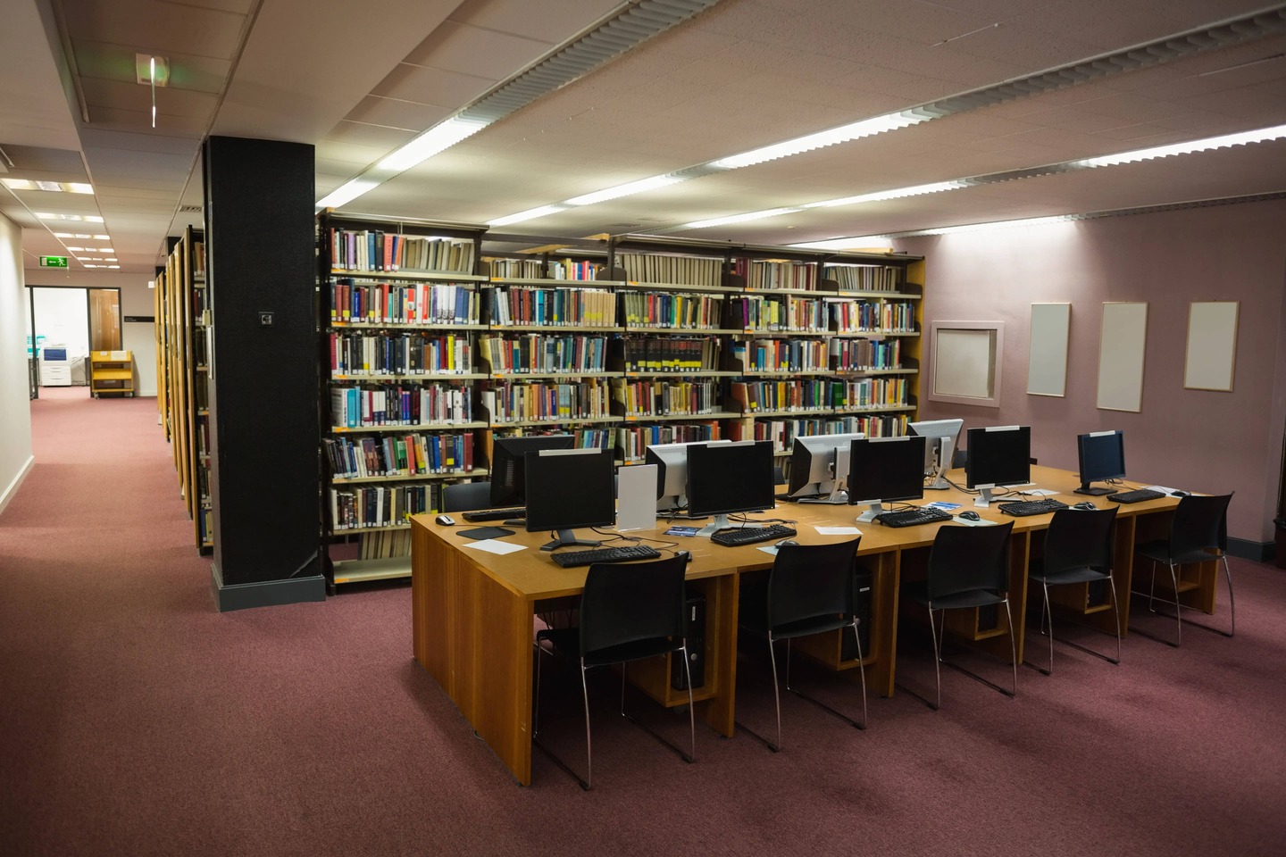 ancada de madeira com fileira de computadores para pesquisa dentro de uma biblioteca.