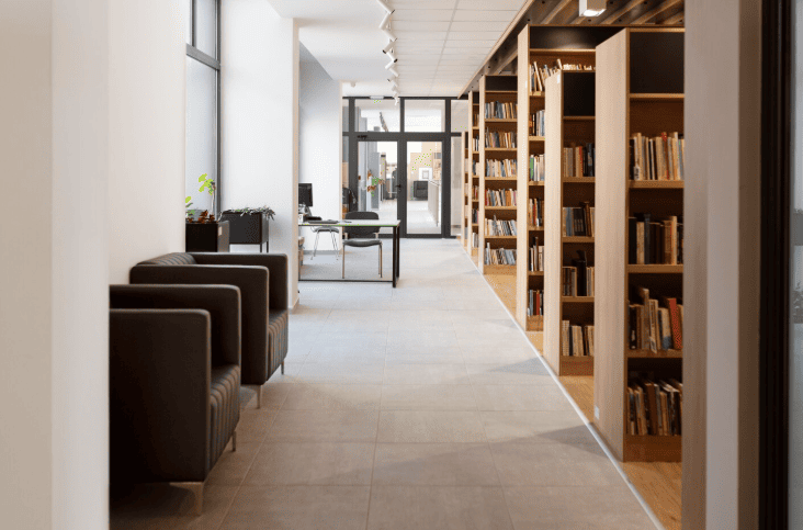 Corredor de biblioteca com poltronas pretas e estantes de madeira cheias de livros.