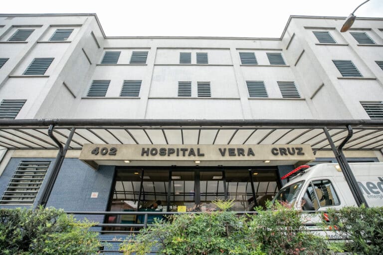  Fachada externa de entrada do Hospital Vera Cruz em Campinas com ambulância estacionada.