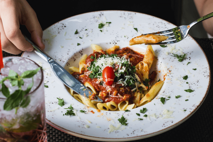 Prato de macarrão penne ao molho de tomate com queijo ralado e manjericão.