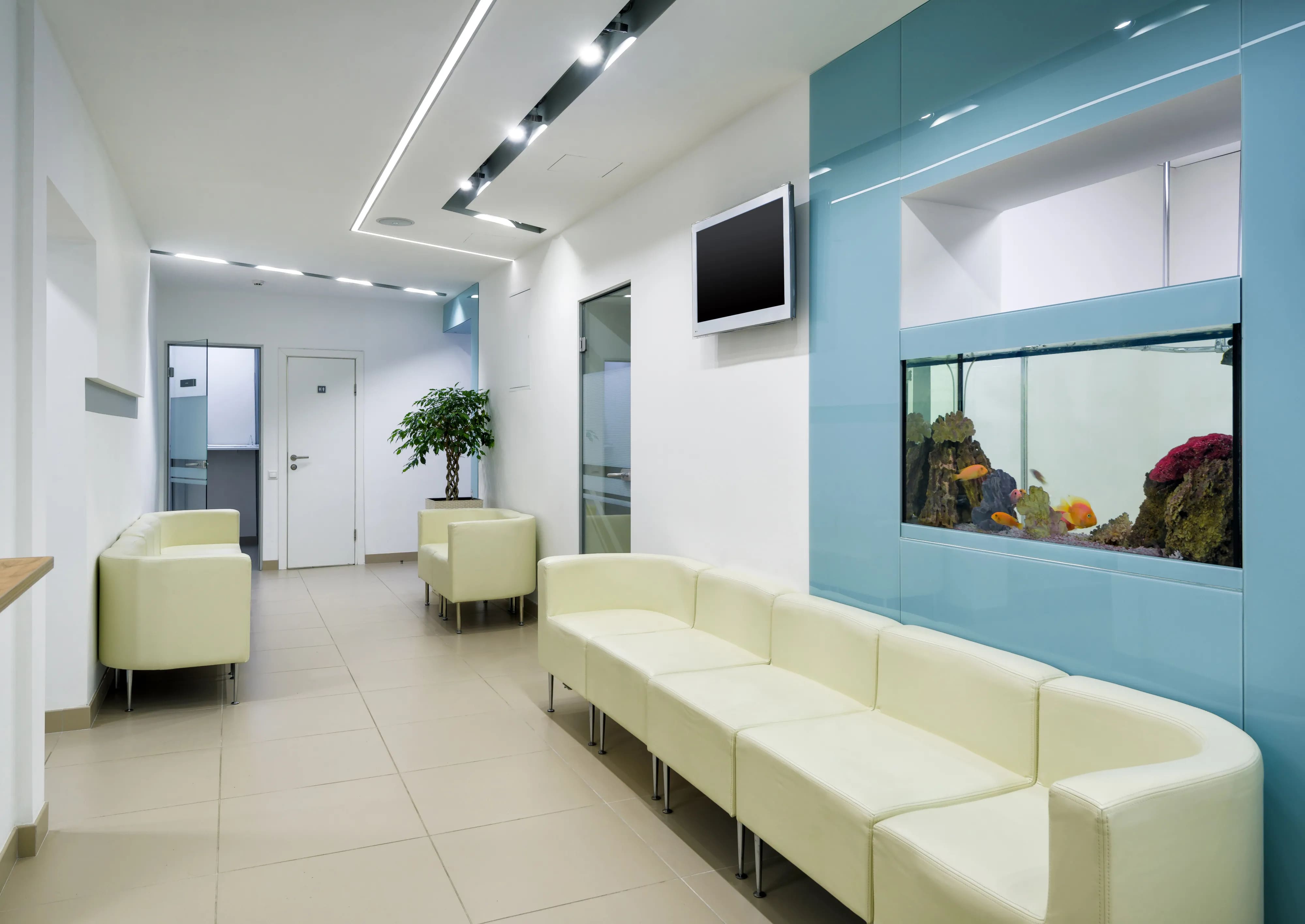 Sala de espera de consultório médico com sofás brancos e um grande aquário embutido na parede azul.