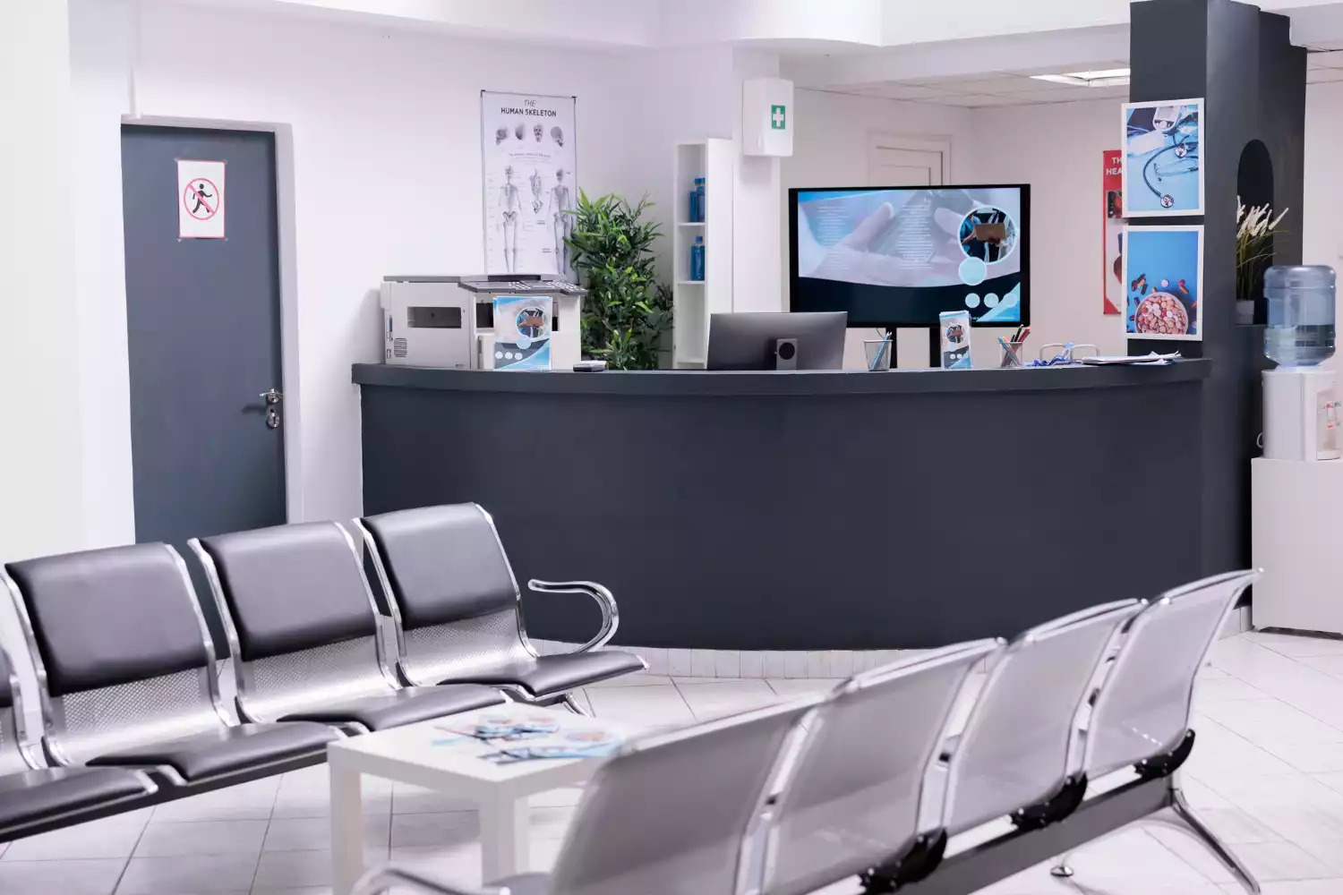 Sala de espera de uma clínica médica com balcão de recepção e cadeiras cinzas.