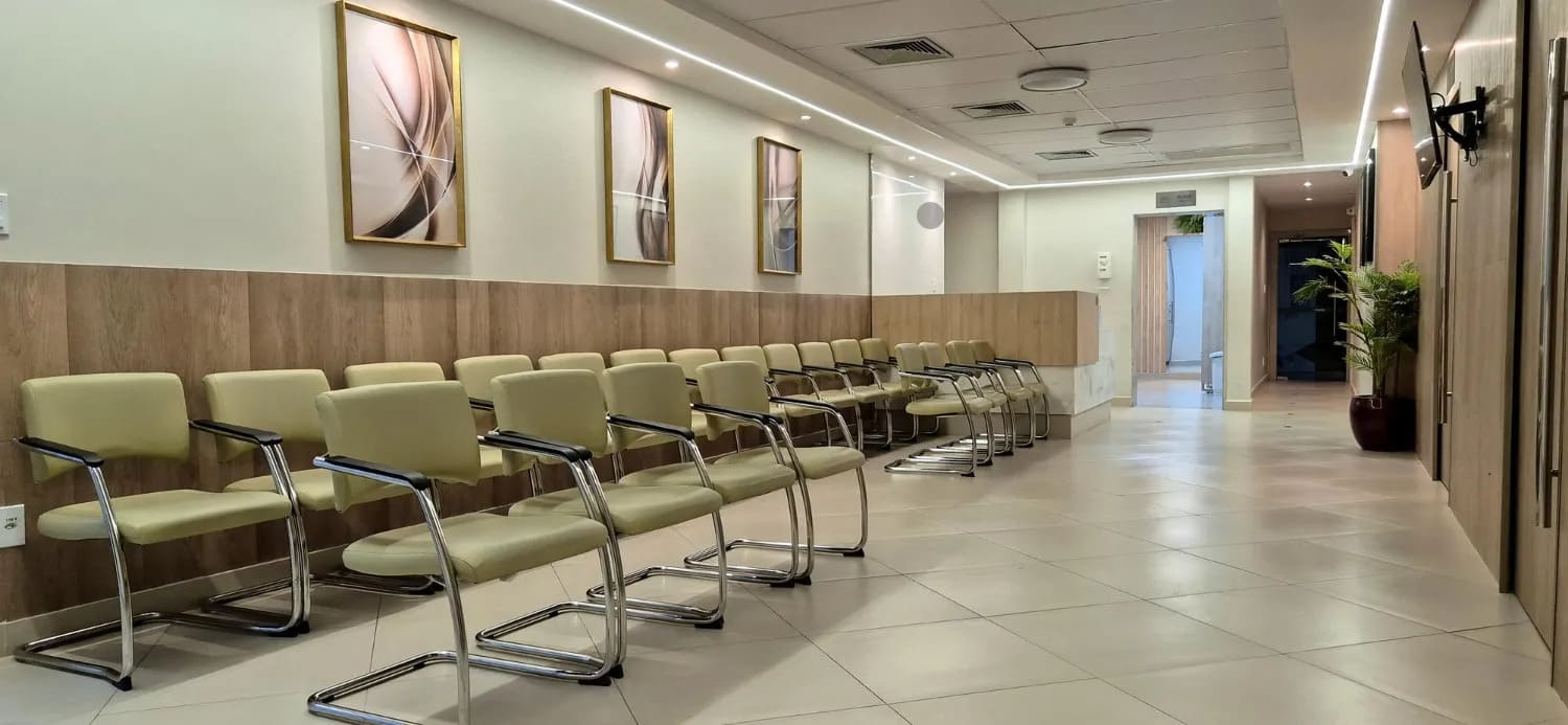 Sala de espera de um consultório moderno com fileiras de cadeiras de couro bege e quadros decorativos.