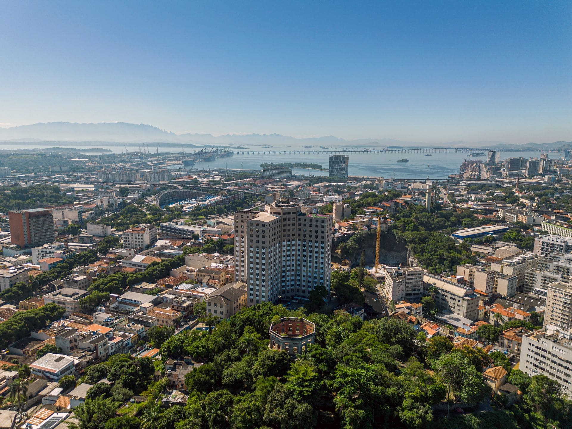 Vista aérea da cidade do Rio de Janeiro com prédios, vegetação e a baía ao fundo.